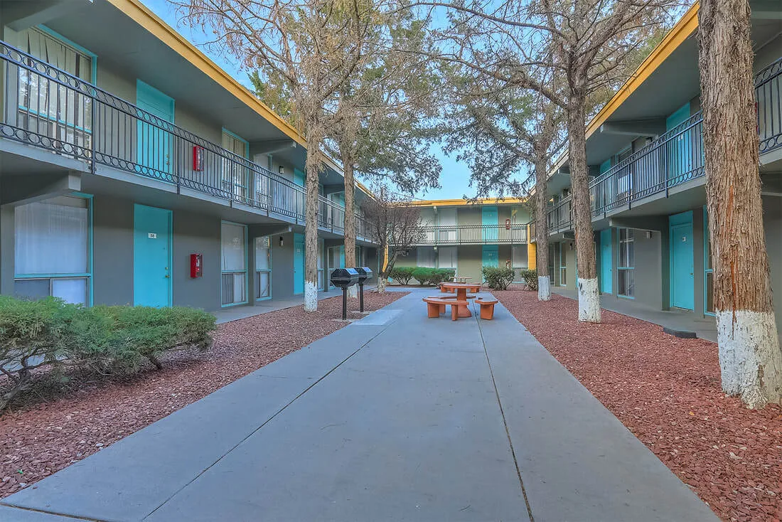 Tree-lined courtyard walkway between two-story buildings at Uptown Horizon Apartments